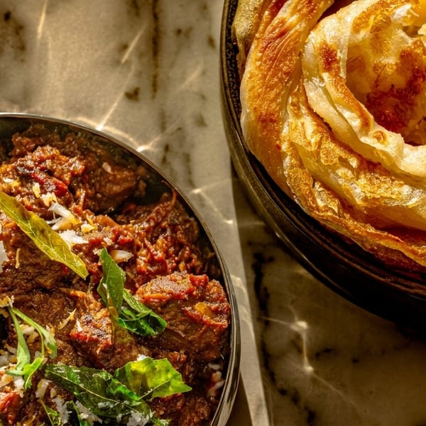 Spicy beef curry with a dried chili and fresh herbs next to flaky paratha bread.