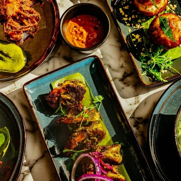 Overhead view of various colorful Indian dishes, including fried seafood, curries, and sauces, on a marble table.